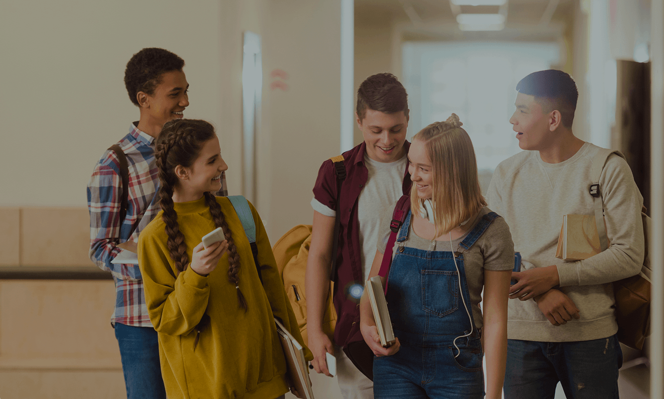 Smiling high school students walking down a school hallway with books